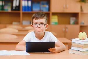 Elementary schoolboy using digital tablet with classmate studying in background at classroom photo