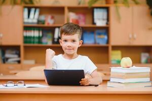 Elementary schoolboy using digital tablet with classmate studying in background at classroom photo