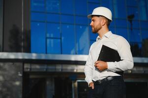 Successful engineer or architect, crane and building construction at backgrpound. Joyous businessman with wearing helmet. photo