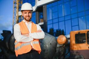 Successful engineer or architect, crane and building construction at backgrpound. Joyous businessman with wearing helmet. photo