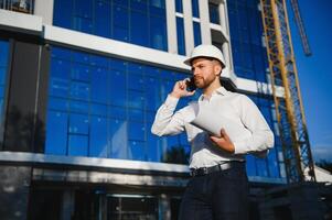 Successful engineer or architect, crane and building construction at backgrpound. Joyous businessman with wearing helmet. photo