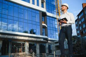 Engineer next to building cranes. Concept - large construction project. Architect directs the construction process. Drawings and tablet in the hands. photo