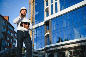 Engineer next to building cranes. Concept - large construction project. Architect directs the construction process. Drawings and tablet in the hands. photo