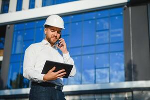 Engineer next to building cranes. Concept - large construction project. Architect directs the construction process. Drawings and tablet in the hands. photo