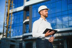 Engineer next to building cranes. Concept - large construction project. Architect directs the construction process. Drawings and tablet in the hands. photo