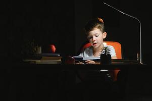 young teenager schoolboy at the table doing homework in the dark room photo