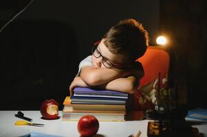 Happy child in eyeglasses reading book at table with lamp. photo