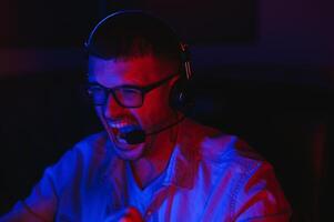 Pro Gamer. Millennial Guy Using Desktop Computer Playing Online Videogame Sitting At Night At Home. Neon Lights, Selective Focus photo