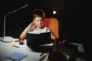 Boy learn lessons in the home setting at the table in the light of a table lamp. photo