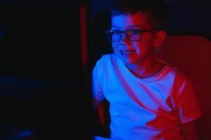Child online broadcasts computer game, boy streams in headphones on rgb lighting background photo