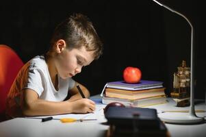 Boy learn lessons in the home setting at the table in the light of a table lamp. photo