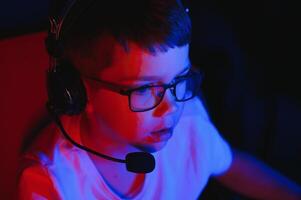 Child online broadcasts computer game, boy streams in headphones on rgb lighting background photo