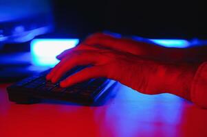 Close-up On Gamer's Hands on a keyboard, Actively Pushing Buttons, Playing MMO Games Online. Background is Lit with Neon Lights. photo