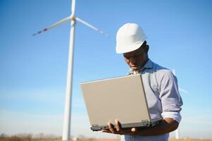 African Engineer standing and hoding laptop with wind turbine photo