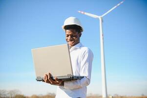 African Engineer standing and hoding laptop with wind turbine photo