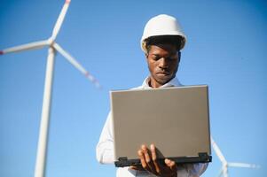 African Engineer standing and hoding laptop with wind turbine photo