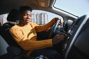Smiling African American young man, sitting in the cabin of a comfortable modern electric car and touching the screen of navigation self-driving autopilot photo