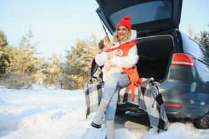 Woman resting in the winter forest sitting in the open trunk of a car with a dog. photo