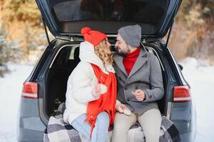 lovely smiling couple sitting in car trunk in winter forest photo
