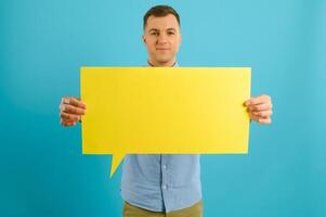 Joyful Caucasian man demonstrating blank placard on blue studio background, mockup for design photo