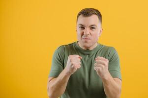 Excited young man guy posing isolated on yellow background studio portrait. People lifestyle concept. Mock up copy space. Rising hands, clenching fists like winner photo
