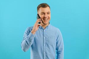 Young man in bright colorful wear talking on mobile cell phone on blue background. Trendy guy have conversation. Smartphone, technology concept. photo