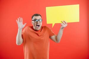 Happy smiling man holding yellow bubble speech, looking at camera over red background photo