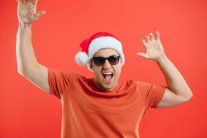 Portrait of happy and excited man in santa hat, rejoicing and winning something, celebrating new year, standing over red background photo