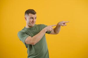 Portrait of a joyful young man pointing fingers away at copy space on his palm isolated over yellow background photo