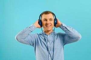 Handsome young man posing on color background. Young smiling man listening to music on headphones. photo