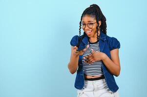 Happy cheerful Afro American woman looks at screen of smart phone enjoys online chatting types text message surfs social networks dressed casually poses against blue background. Technology concept. photo