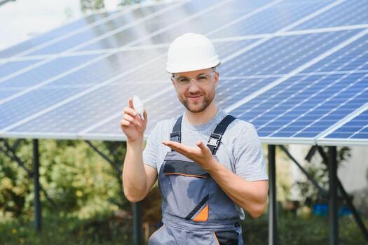 Technical expert in solar photovoltaic panels, remote control performs routine actions to monitor the system using clean renewable energy in the hand a light bulb. photo