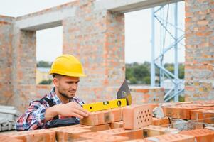 Using bricks. Young construction worker in uniform is busy at the unfinished building photo