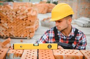 Using bricks. Young construction worker in uniform is busy at the unfinished building photo