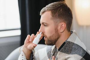 Sick man with nasal spray and paper tissue at home photo