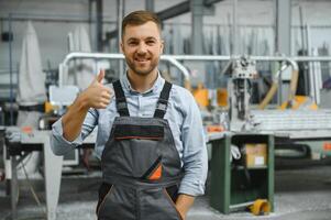 Portrait of factory worker in protective uniform and hardhat standing by industrial machine at production line. People working in industry photo