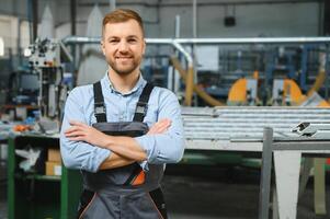 Portrait of factory worker in protective uniform and hardhat standing by industrial machine at production line. People working in industry photo