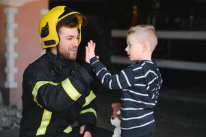 Portrait of rescued little boy with firefighter man standing near fire truck. Firefighter in fire fighting operation. photo