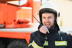 Fireman in a protective uniform standing next to a fire truck and talking on the radio. photo