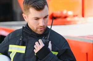 Fireman in a protective uniform standing next to a fire truck and talking on the radio. photo