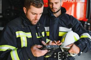 Portrait of two firefighters in fire fighting operation, fireman in protective clothing and helmet using tablet computer in action fighting photo