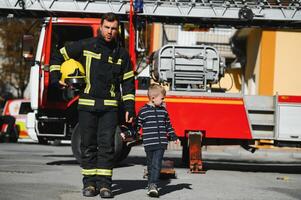 A firefighter take a little child boy to save him. Fire engine car on background. Fireman with kid in his arms. Protection concept. photo