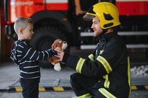Dirty firefighter in uniform holding little saved boy standing on black background. photo