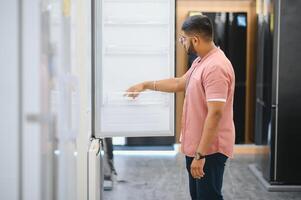 Smart modern indian male customer choosing large fridges in domestic appliances section photo