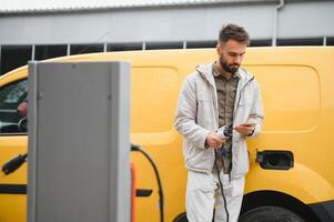 Portrait of a young man standing with charging cable near the charging station photo