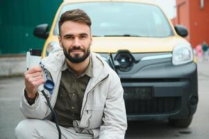 Portrait of a young man standing with charging cable near the charging station photo