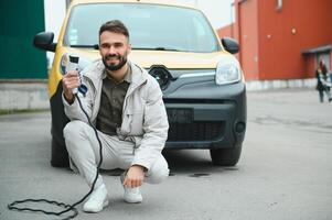 Man Holding Power Charging Cable For Electric Car In Outdoor Car Park. And he s going to connect the car to the charging station in the parking lot near the shopping center photo