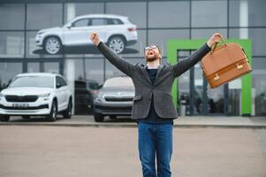Happy buyer near the car in front of the modern avtosalon building photo