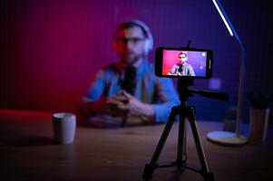 vlogger using smartphone to film podcast in studio. blogger with mobile phone, microphone and headphones filming for social media broadcasting career. photo