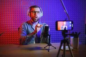 vlogger using smartphone to film podcast in studio. blogger with mobile phone, microphone and headphones filming for social media broadcasting career. photo